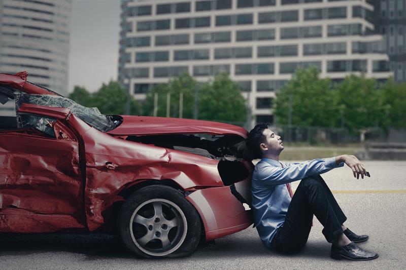 Man sitting beside a damaged car after an accident